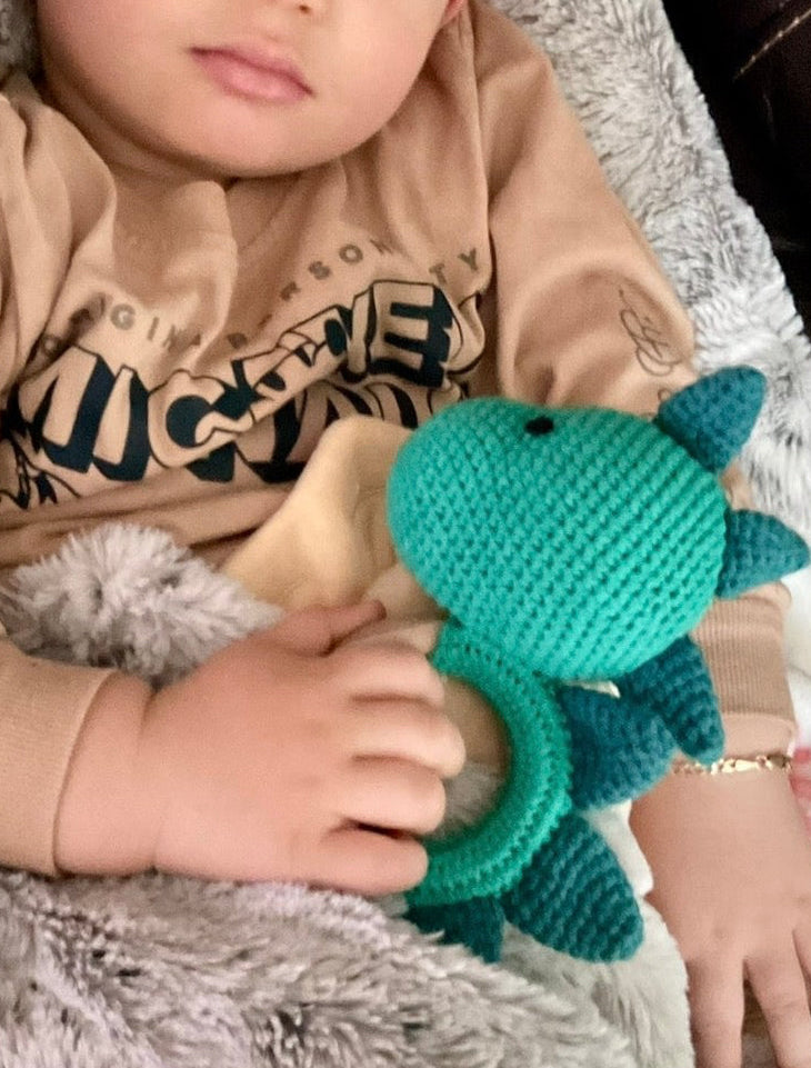 Baby sleeping peacefully while cuddling a handmade teal crochet dinosaur teether toy by Knitted Friends, wrapped in a soft gray blanket