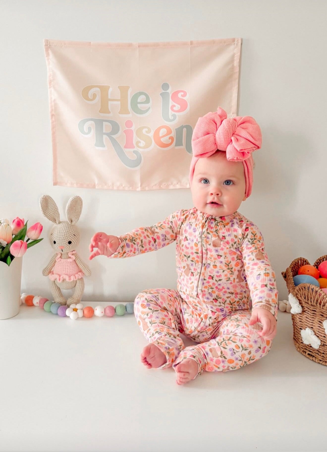 Baby in a floral outfit sitting beside a handmade crochet bunny doll with a pink tutu made by Knitted Friends