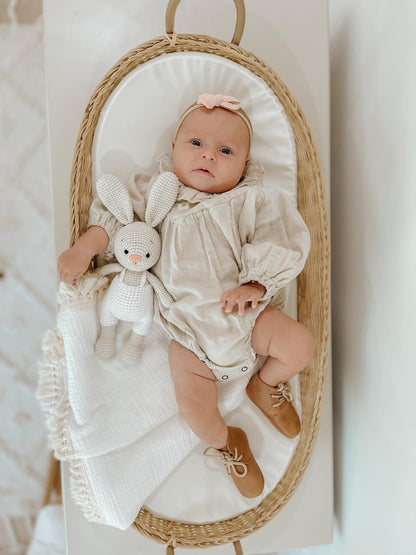 BUNNY WITH OVERALLS HANDMADE . BABY IS HOLDING DOLL IN A BASSINET LOOKING UP .
