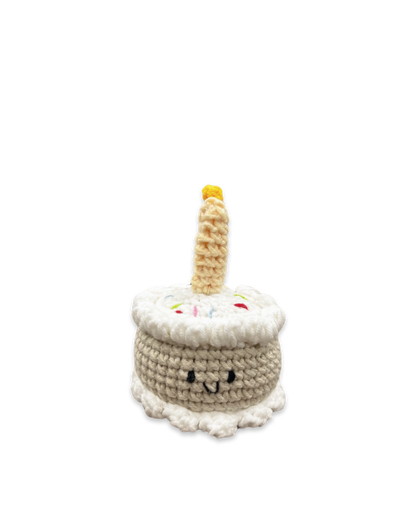 Handmade crocheted birthday cake toy with smiling face, white frosting, sprinkles, and a single candle on top crafted by Knitted Friends