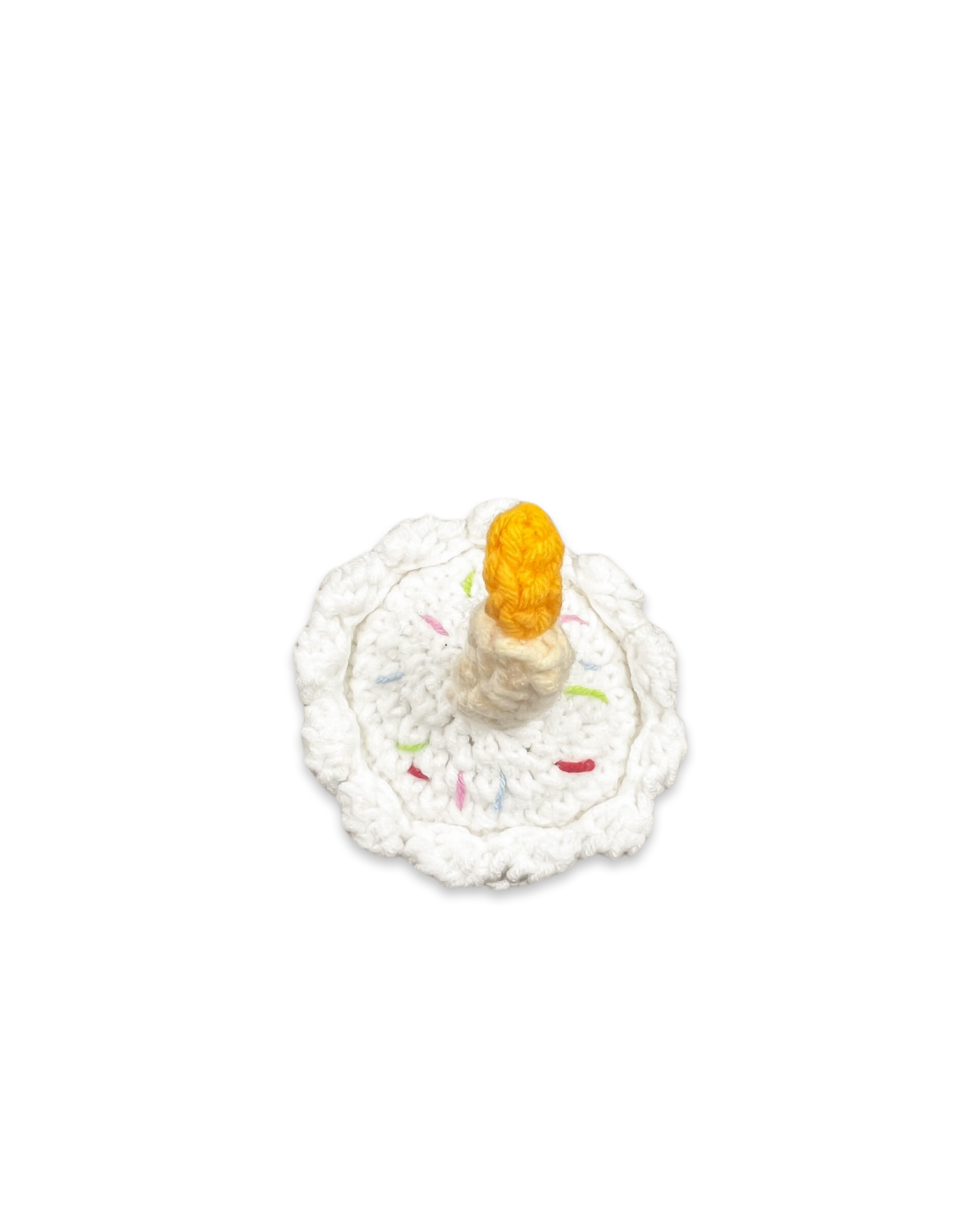 Top view of handmade crocheted birthday cake toy with white frosting, colourful sprinkles, and a single candle crafted by Knitted Friends