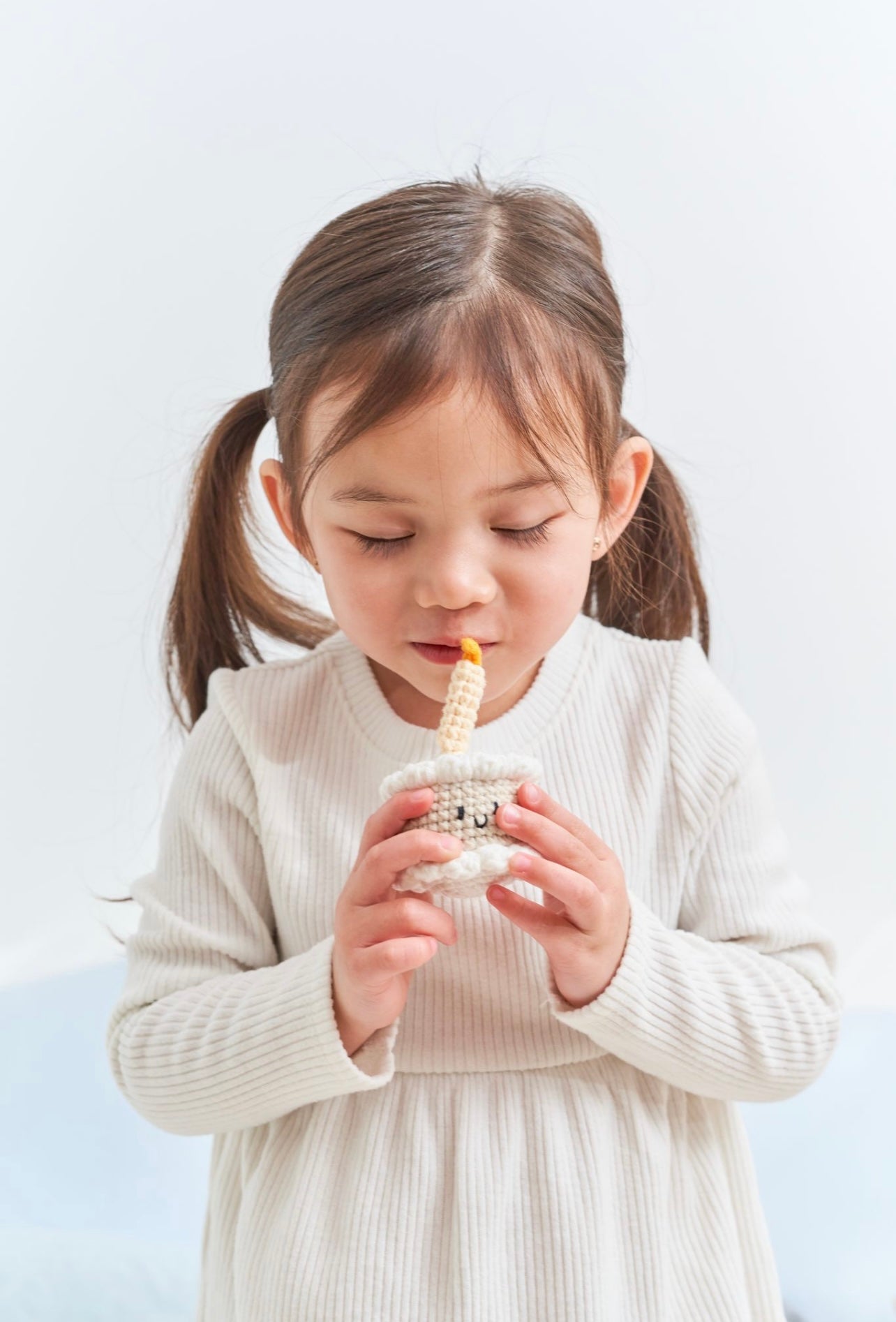 Young girl holding a small crocheted birthday cake toy with a candle made by Knitted Friends, gently pretending to blow it out