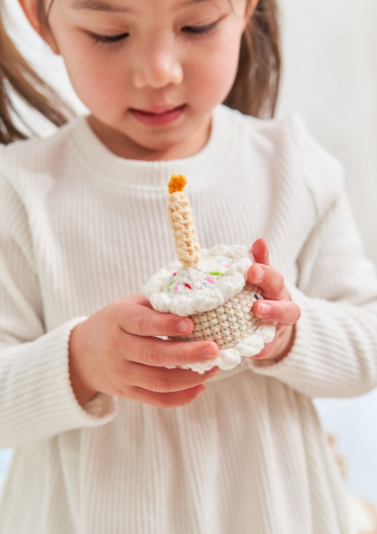 Close-up of young girl holding a handmade crocheted birthday cake toy with candle and sprinkles crafted by Knitted Friends