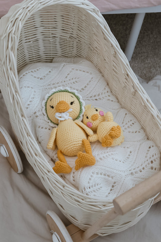 Handmade crochet duck toy doll made by Knitted Friends resting in a white wicker bassinet 
