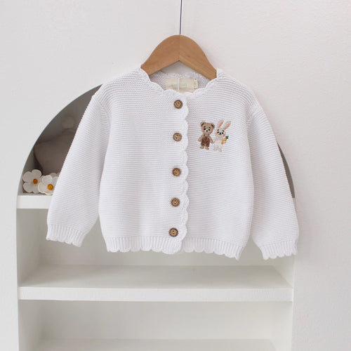 Knitted Friends white baby cardigan with scalloped edges and embroidered bear and bunny, wooden buttons, displayed in a nursery setting