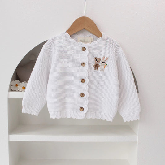 Knitted Friends white baby cardigan with scalloped edges and embroidered bear and bunny, wooden buttons, displayed in a nursery setting