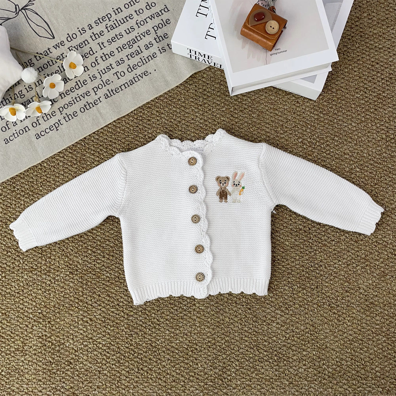 Knitted Friends white baby cardigan with scalloped edges and embroidered bear and bunny, wooden buttons, displayed in a nursery setting