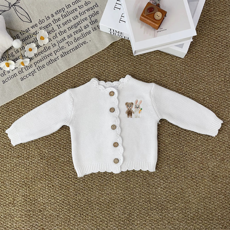 Knitted Friends white baby cardigan with scalloped edges and embroidered bear and bunny, wooden buttons, displayed in a nursery setting