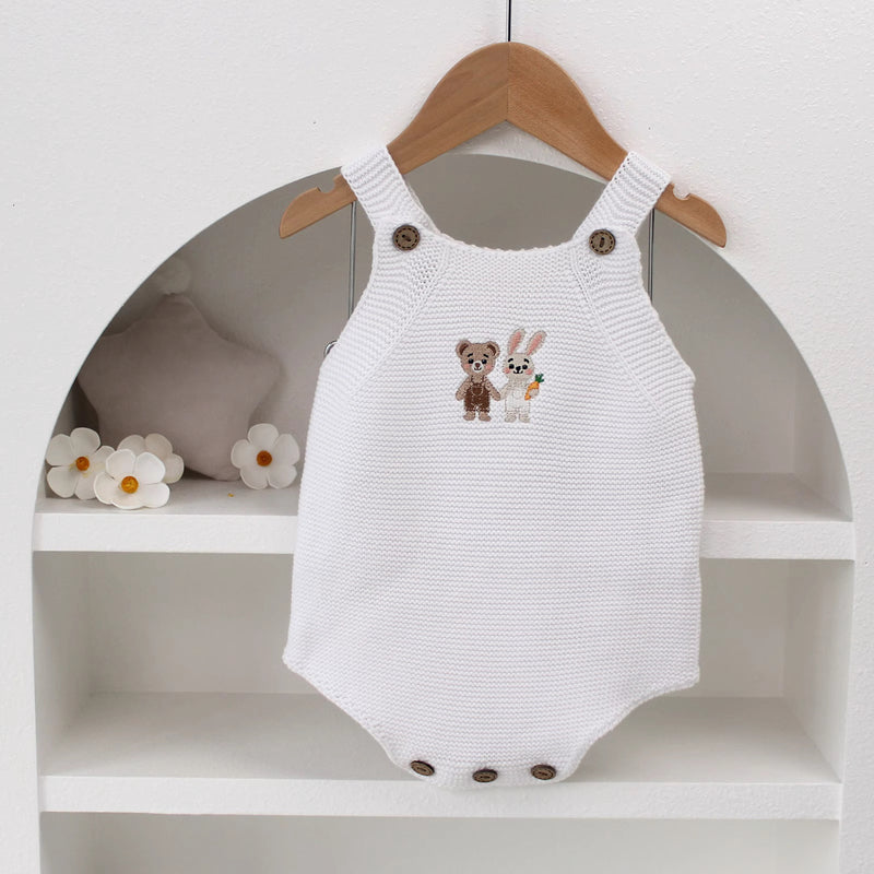 Knitted Friends white baby romper with embroidered bear and bunny, wooden button straps, displayed in a soft nursery setting