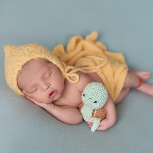 Sleeping newborn baby holding a small crocheted turtle toy made by Knitted Friends