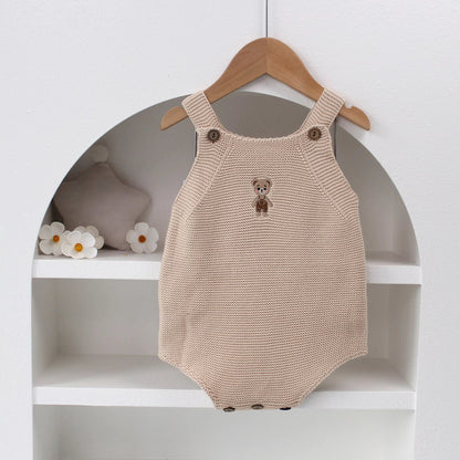 Knitted Friends beige baby onesie with embroidered bear, wooden button straps, displayed in a soft nursery setting