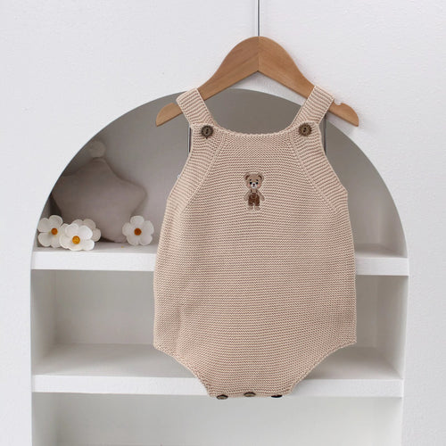 Knitted Friends beige baby onesie with embroidered bear, wooden button straps, displayed in a soft nursery setting