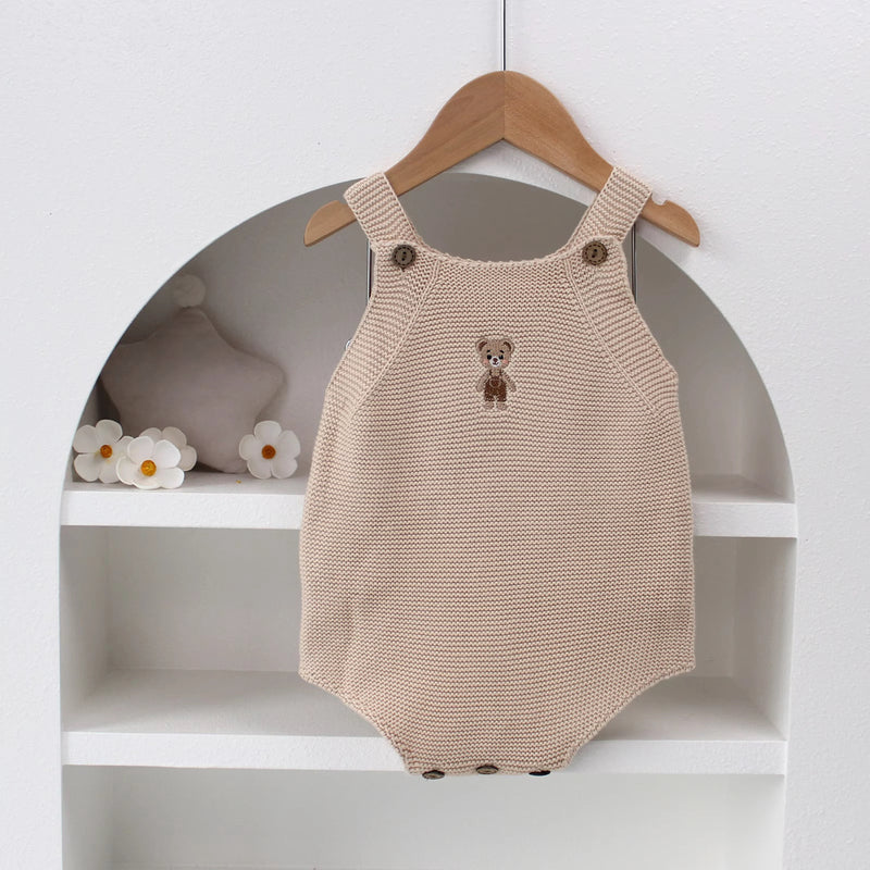 Knitted Friends beige baby onesie with embroidered bear, wooden button straps, displayed in a soft nursery setting