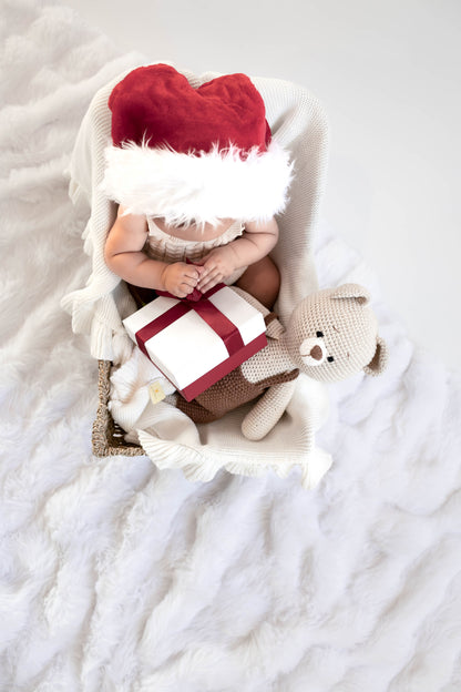Baby wearing Santa hat holding gift box with handmade crochet teddy bear toy by Knitted Friends