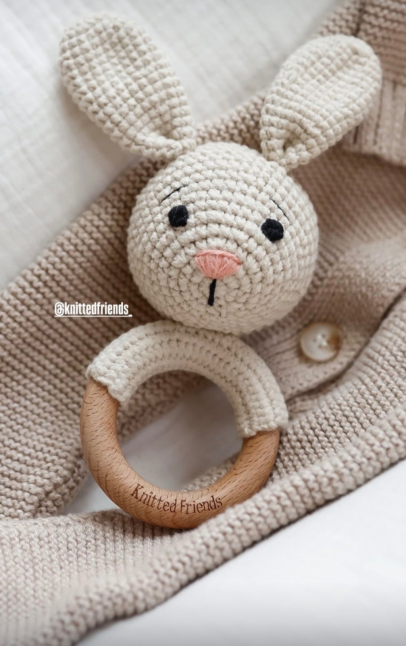 Knitted bunny rattle with wooden ring on a textured fabric background