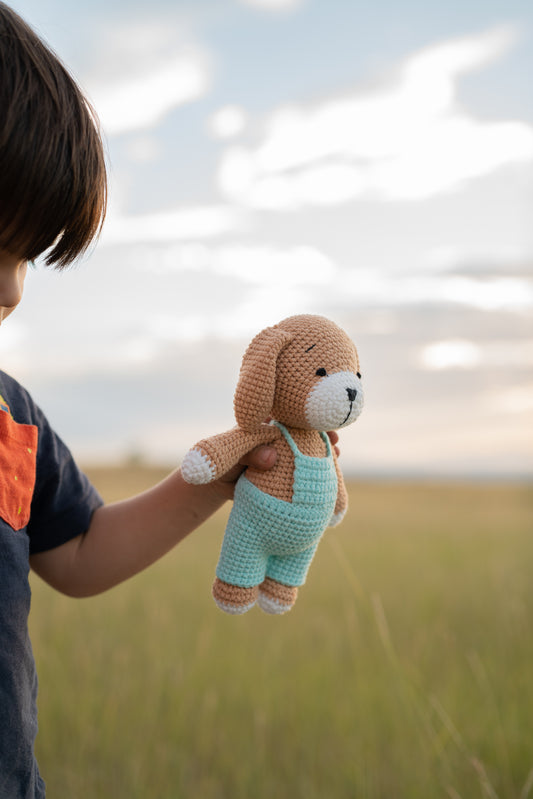 Child holding a handmade crocheted puppy doll in mint overalls made by Knitted Friends