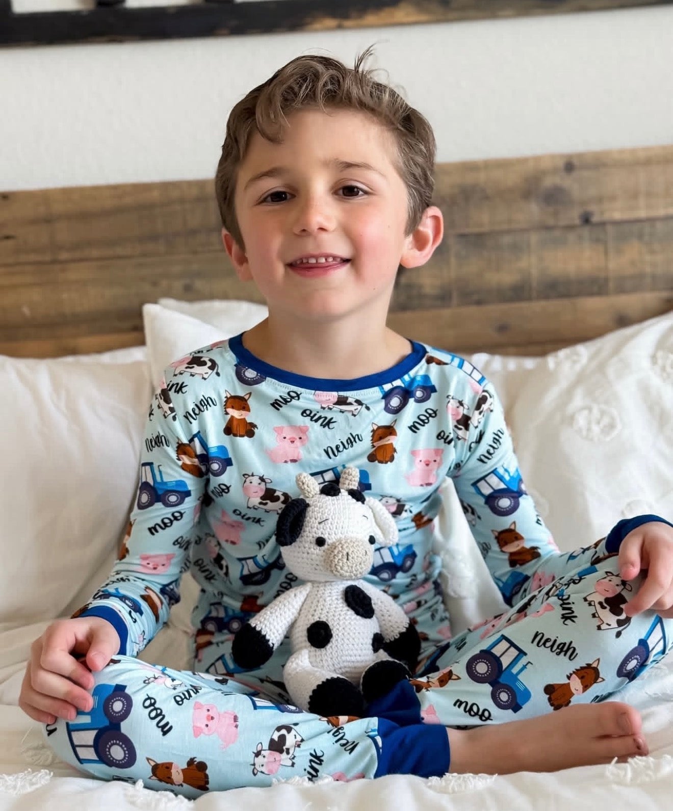 Young boy sitting holding a handmade crochet cow doll by Knitted Friends