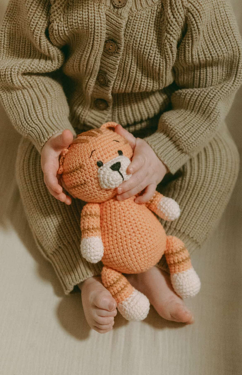 Baby holding an orange crocheted tiger doll by Knitted Friends