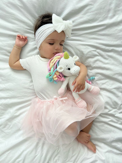 Baby hugging a handmade crochet unicorn doll by Knitted Friends