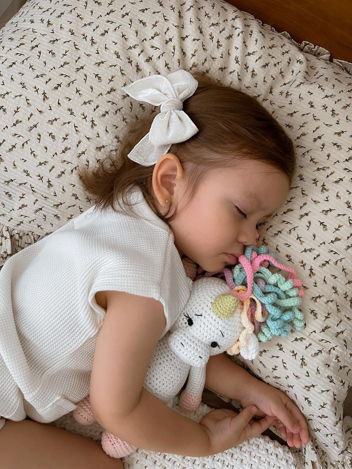 Toddler cuddling a handmade crochet unicorn doll made by Knitted Friends