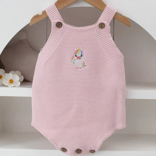 Knitted Friends pink baby onesie with embroidered unicorn, wooden button straps, displayed in a soft nursery setting.