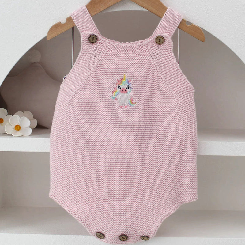 Knitted Friends pink baby onesie with embroidered unicorn, wooden button straps, displayed in a soft nursery setting.